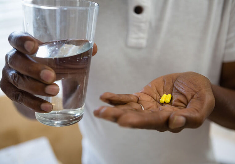 A man is taking two pills with water.